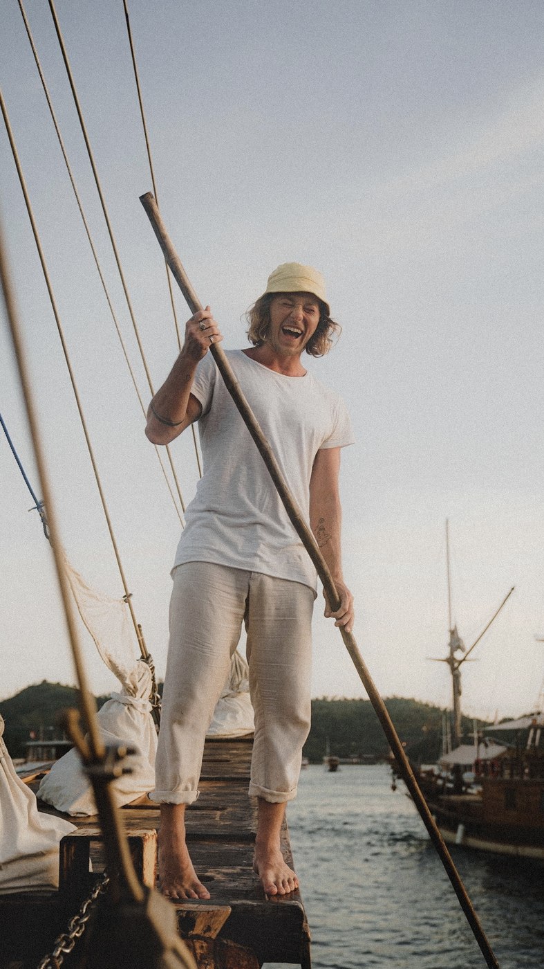 Jaro laughing solo on the bow of a sailboat at sunset