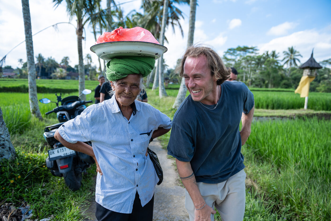 Jaro walking and laughing with a local elderly woman beside a rice paddy