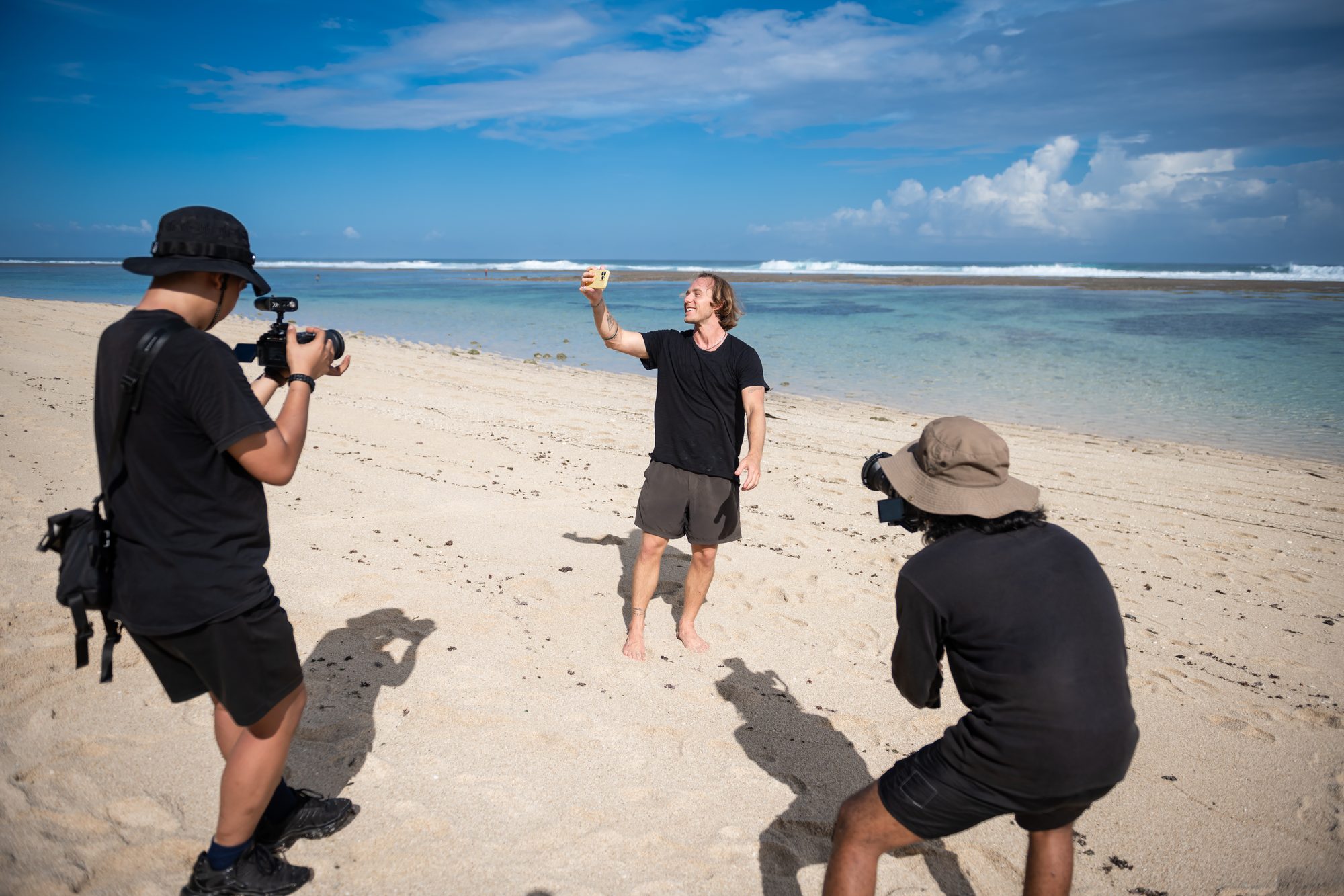Jaro filming a selfie video on a beach with two crew members shooting behind him