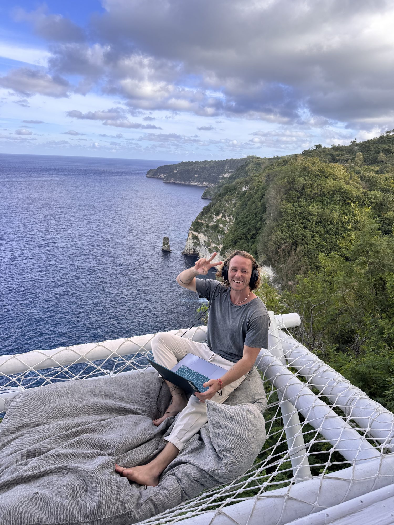 Jaro working on his laptop from a hammock overlooking cliffs and the ocean