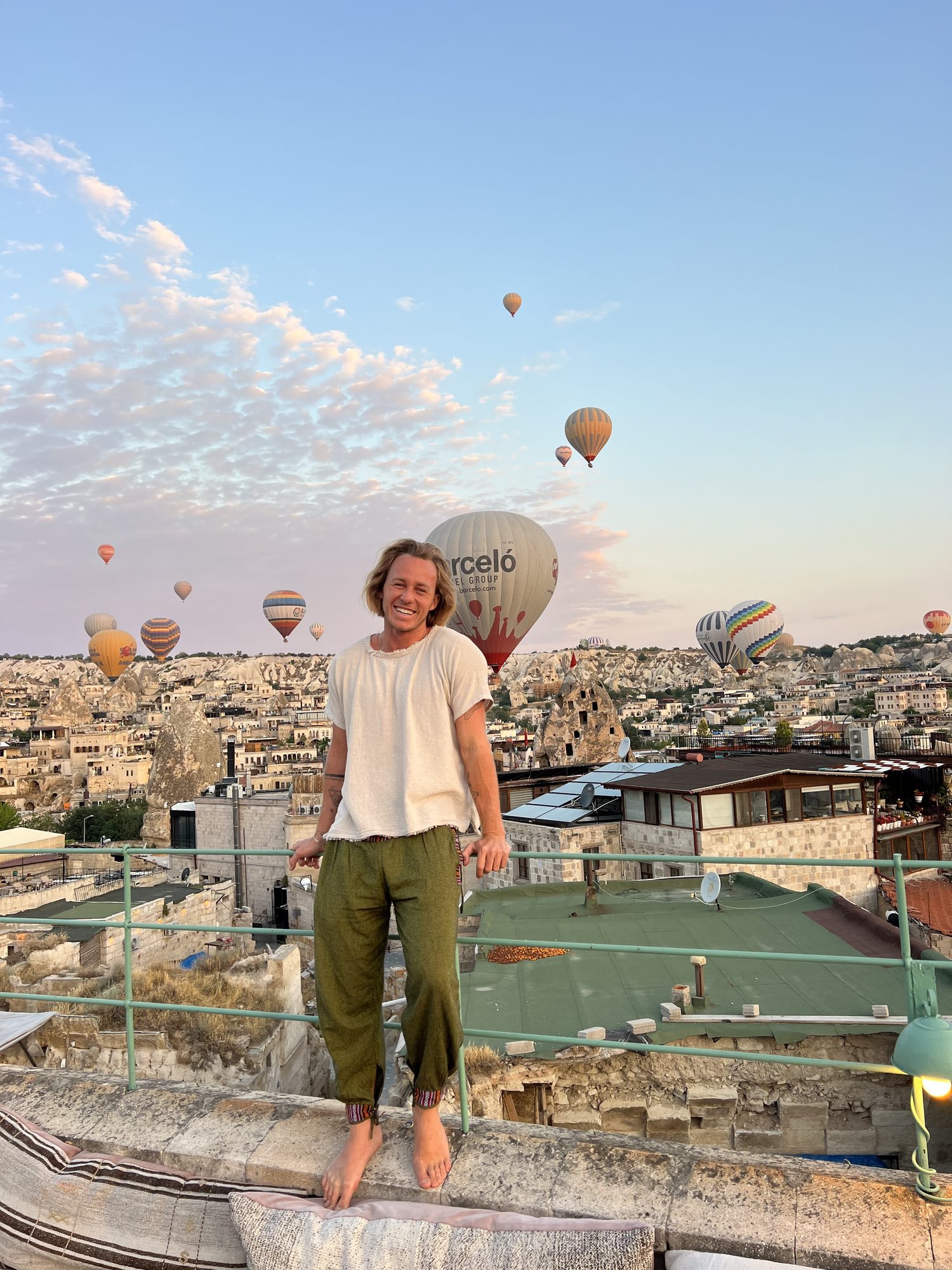 Jaro smiling on a rooftop in Cappadocia as dozens of hot air balloons rise behind him at sunrise