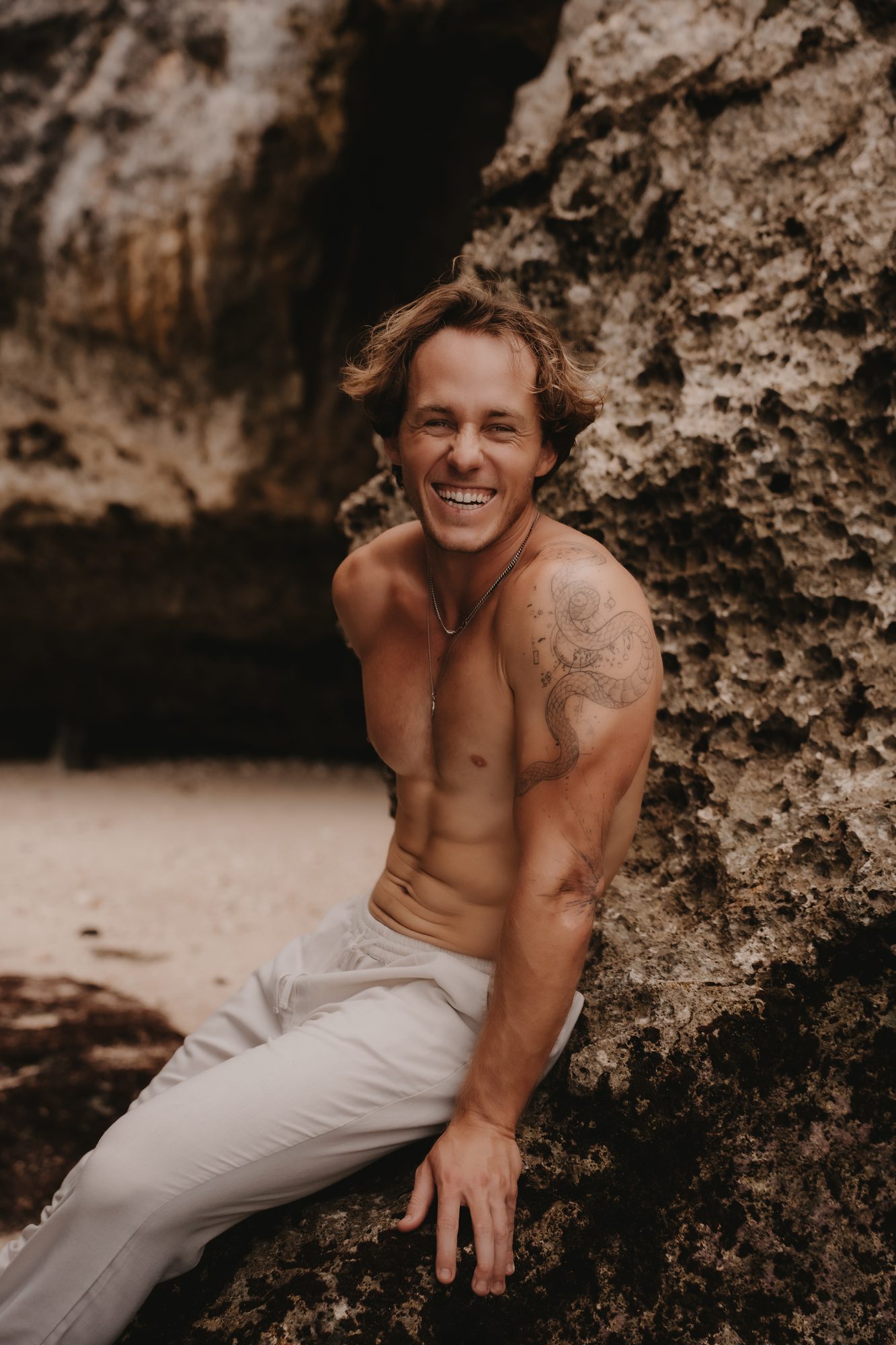 Close portrait of Jaro smiling, seated against a cave rock face at the beach