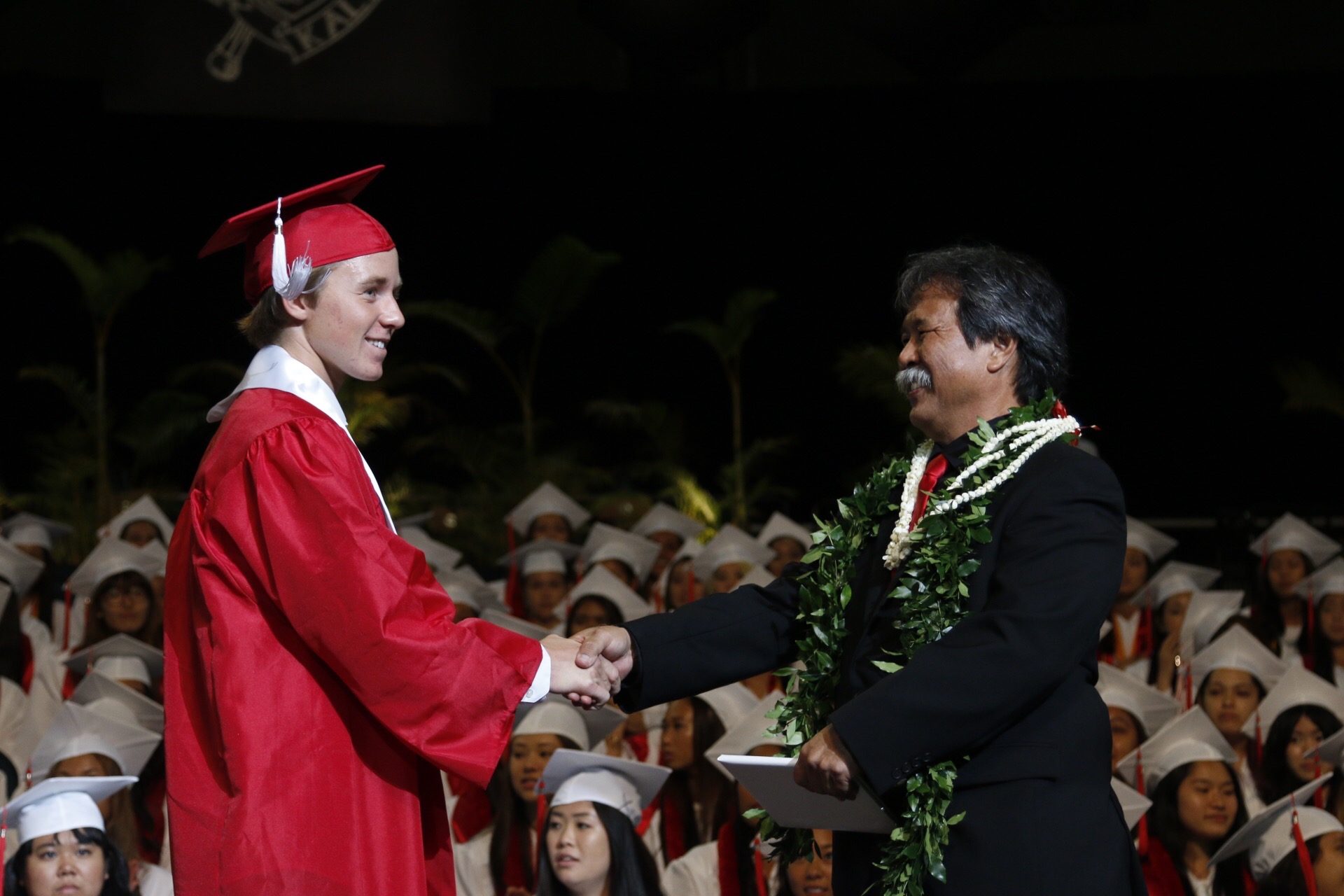 A young Jaro in a red cap and gown shaking hands at his high school graduation in Hawaii